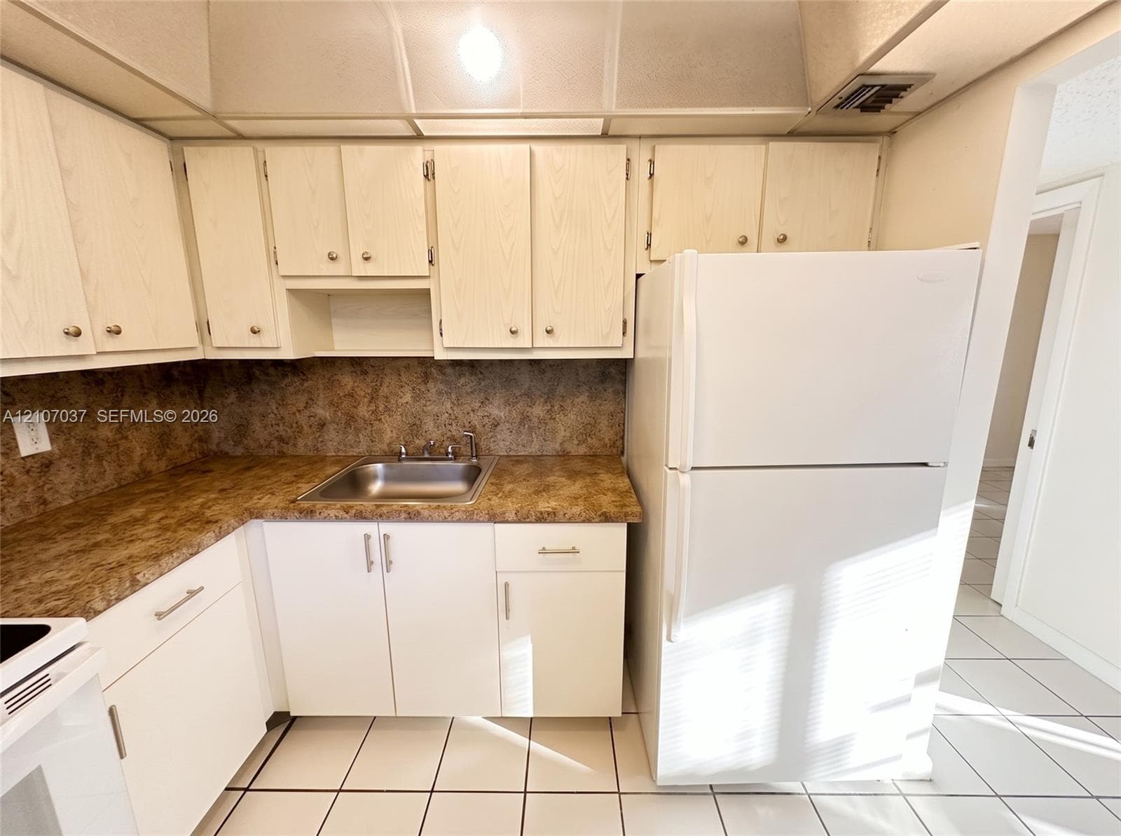 Kitchen featuring light-finish cabinetry, patterned laminate countertops, stainless steel drop-in sink, and ceramic tile flooring