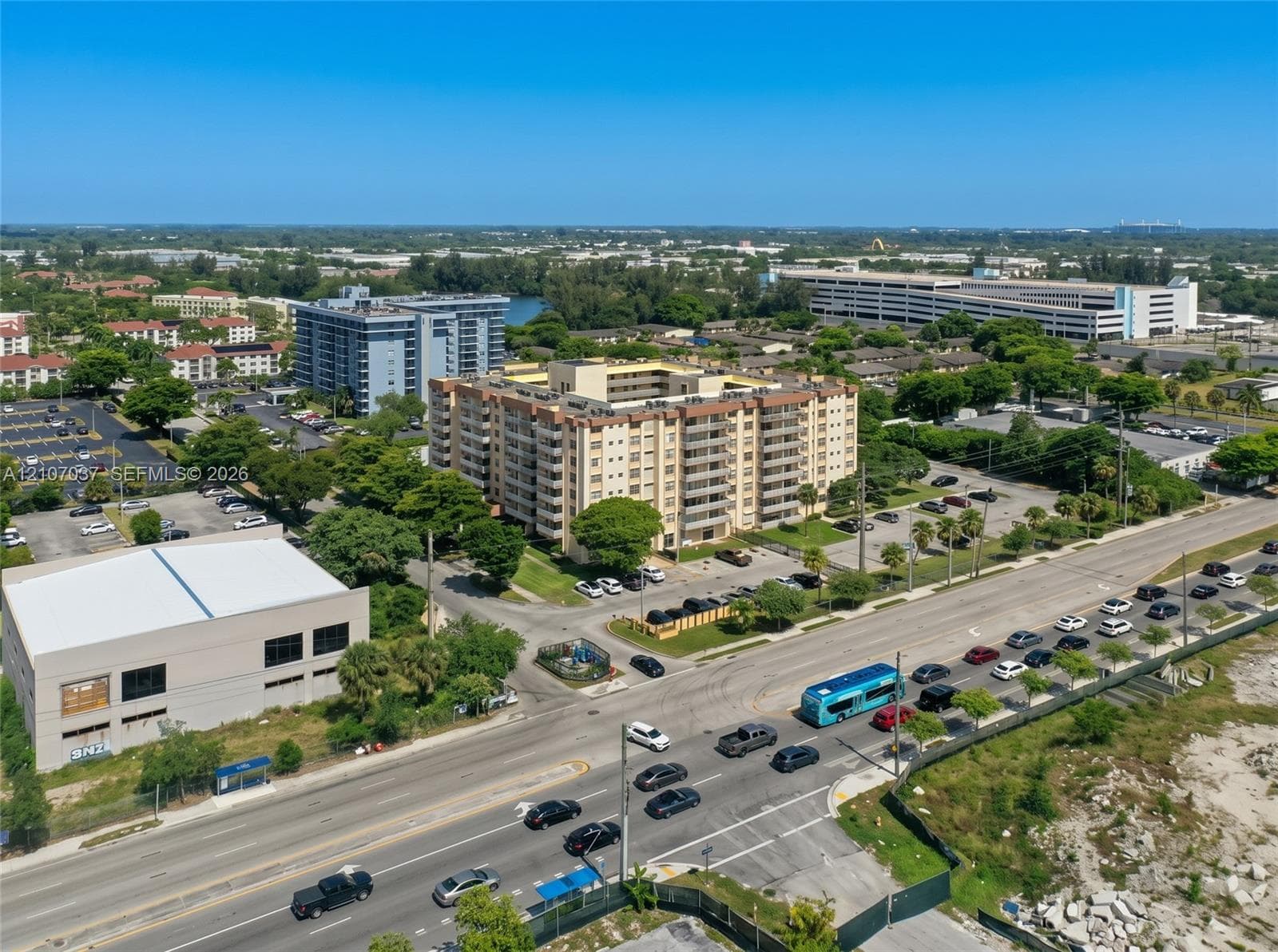 Multi-story residential complex featuring beige stucco exterior, private balconies, on-site surface parking, and mature landscaping