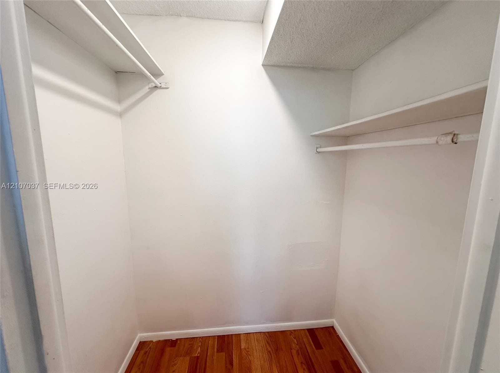 Reach-in closet featuring wood-finish flooring and dual tiers of built-in shelving with integrated rods