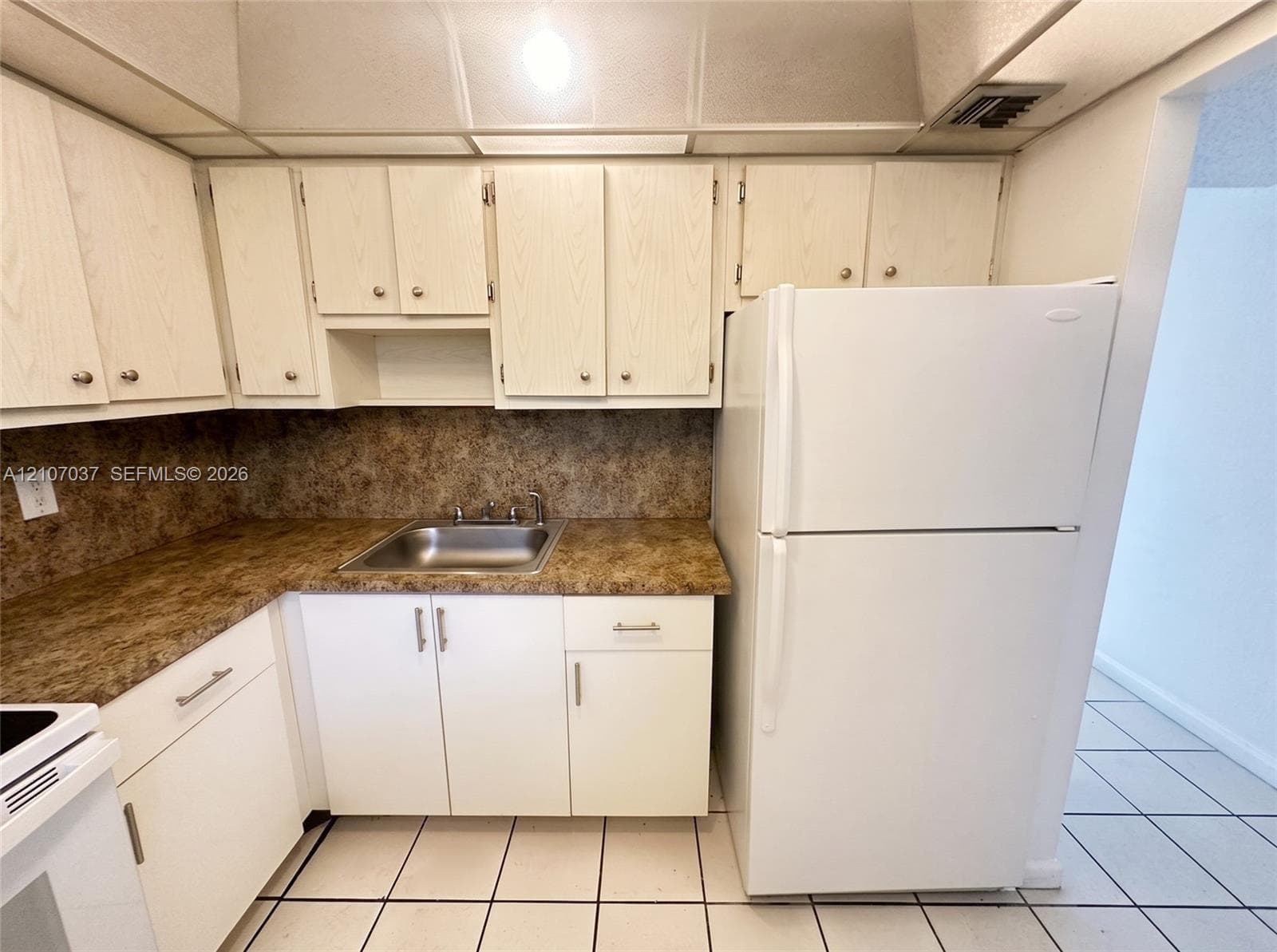 Kitchen featuring light-finish cabinetry, stone-patterned laminate countertops, stainless steel sink with dual-handle faucet, ceramic tile flooring, and integrated lighting