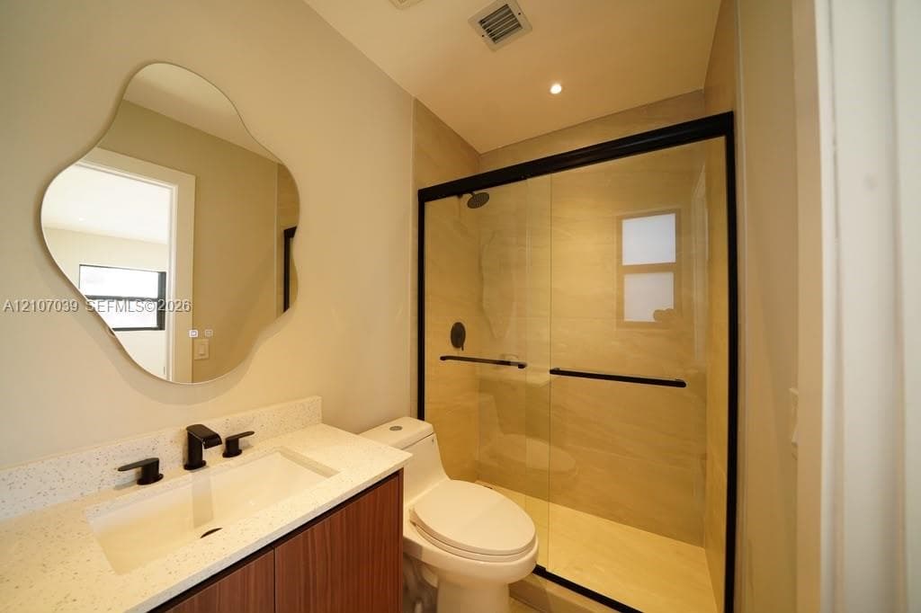 Floating vanity with a light-toned stone countertop, uniquely shaped wall-mounted mirror, matte black plumbing fixtures, and walk-in shower with a glass enclosure