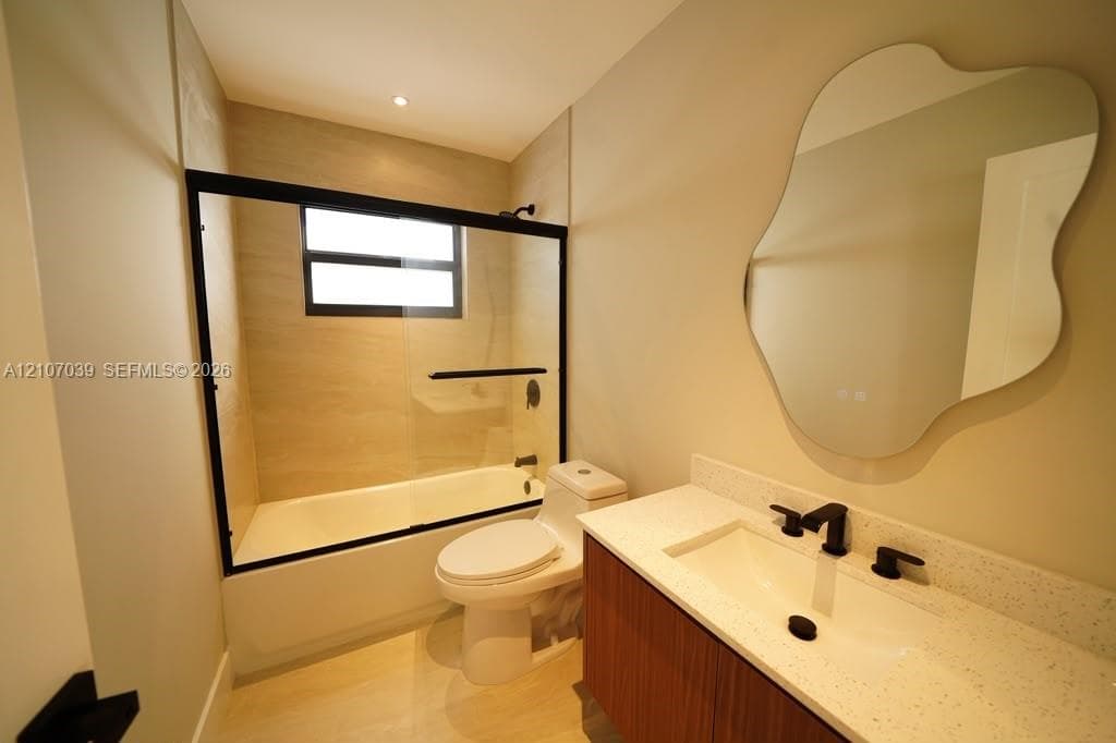 Floating vanity with light-colored speckled countertop, undermount sink, matte black widespread faucet, organic-shaped wall mirror, and tub-shower combination featuring a black-framed glass enclosure