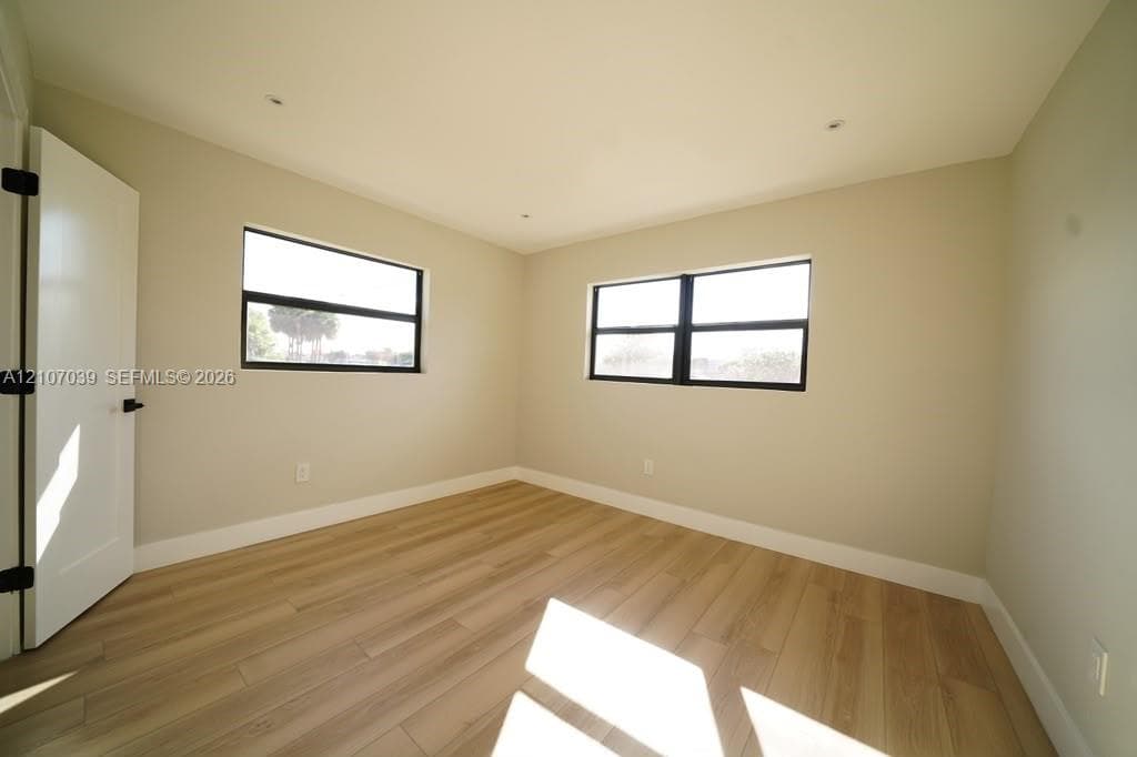 Neutral interior space featuring wood-finish flooring, dual windows with dark frames, recessed lighting, and a shaker-style interior door with matte black hardware