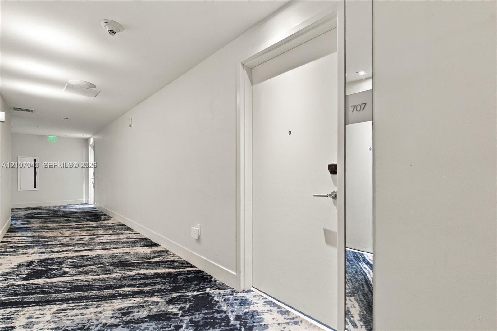 Hallway featuring patterned wall-to-wall carpeting, recessed ceiling lighting, and a white entry door equipped with a digital keypad lock