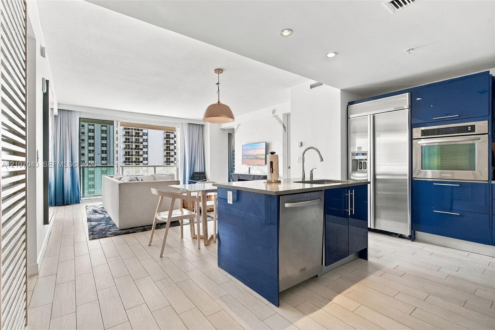 Kitchen featuring high-gloss blue cabinetry, stainless steel appliances, a kitchen island with an undermount sink, and light-toned tile flooring
