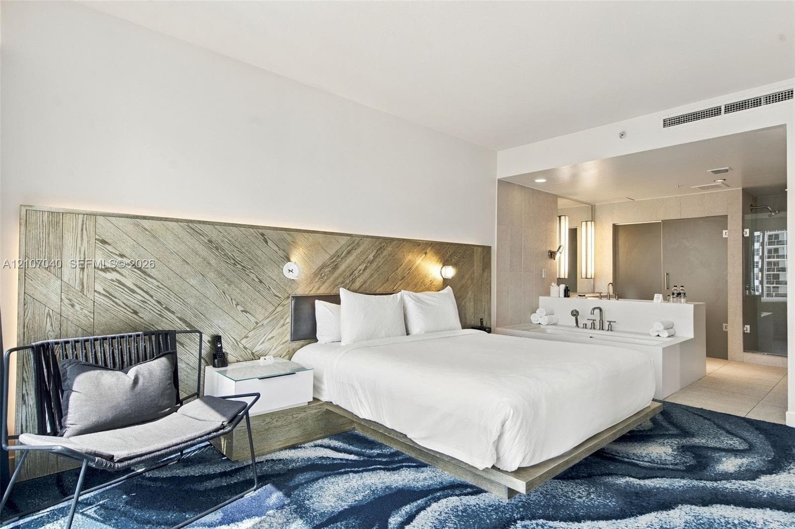 Diagonally patterned wood-finish headboard, built-in floating bed frame, integrated bedside tables, and open-concept bathroom featuring a soaking tub