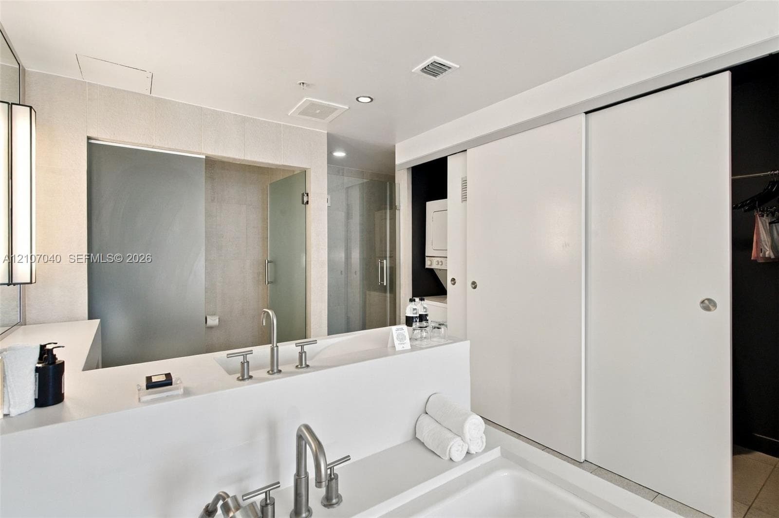 Modern bathroom featuring a rectangular vessel sink with a bridge-style faucet, white solid-surface countertop, walk-in glass shower enclosure, and sliding panel doors