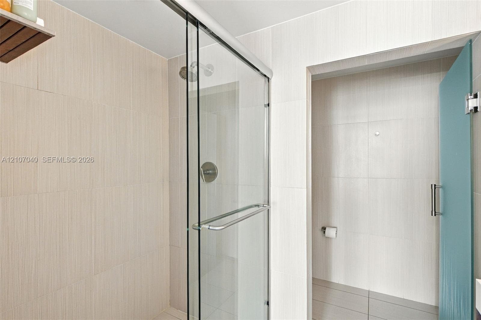 Walk-in shower featuring floor-to-ceiling neutral tile, a frameless glass sliding door, polished chrome fixtures, and a glass-paneled entry door