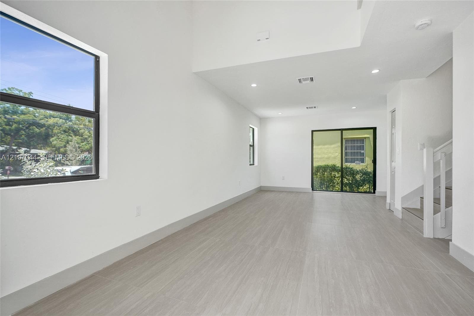 Open-concept interior featuring high ceilings, wood-finish flooring, recessed lighting, large dual-pane windows, and sliding glass doors