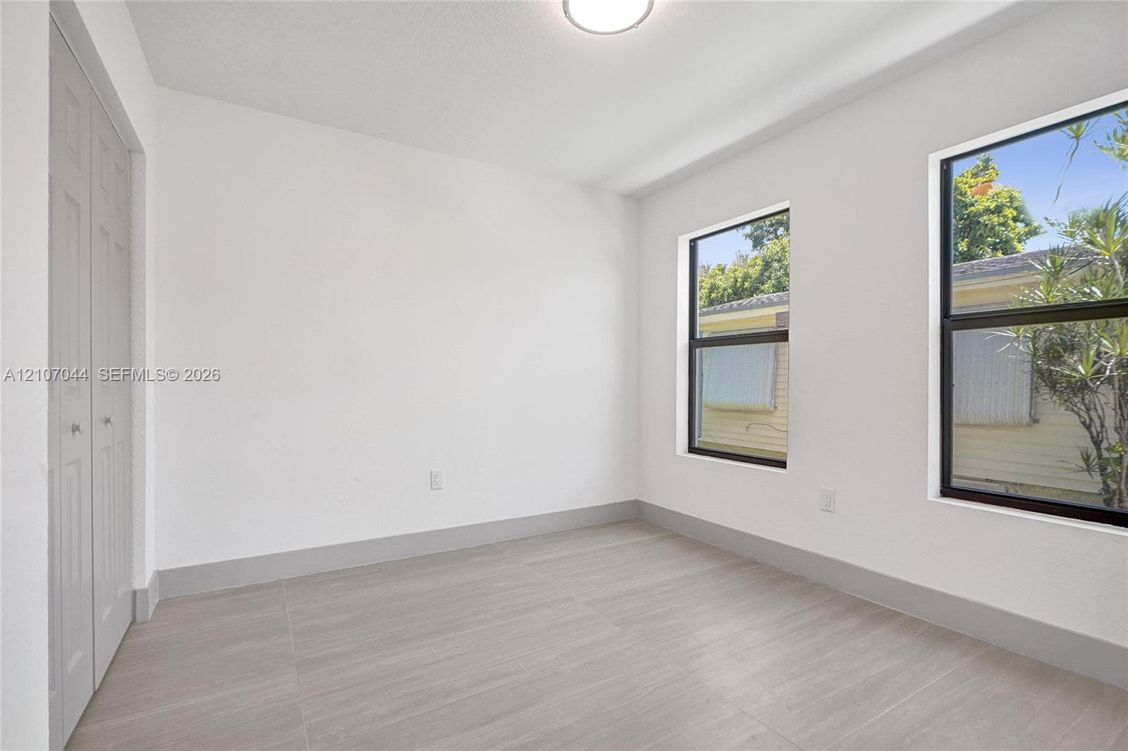 Neutral-toned interior featuring oversized tile flooring, dual-panel closet doors, and black-framed windows