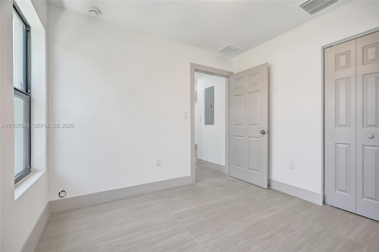 Neutral-toned interior featuring wood-finish flooring, a six-panel swing door, a bi-fold closet door, and a single-hung window with a deep sill