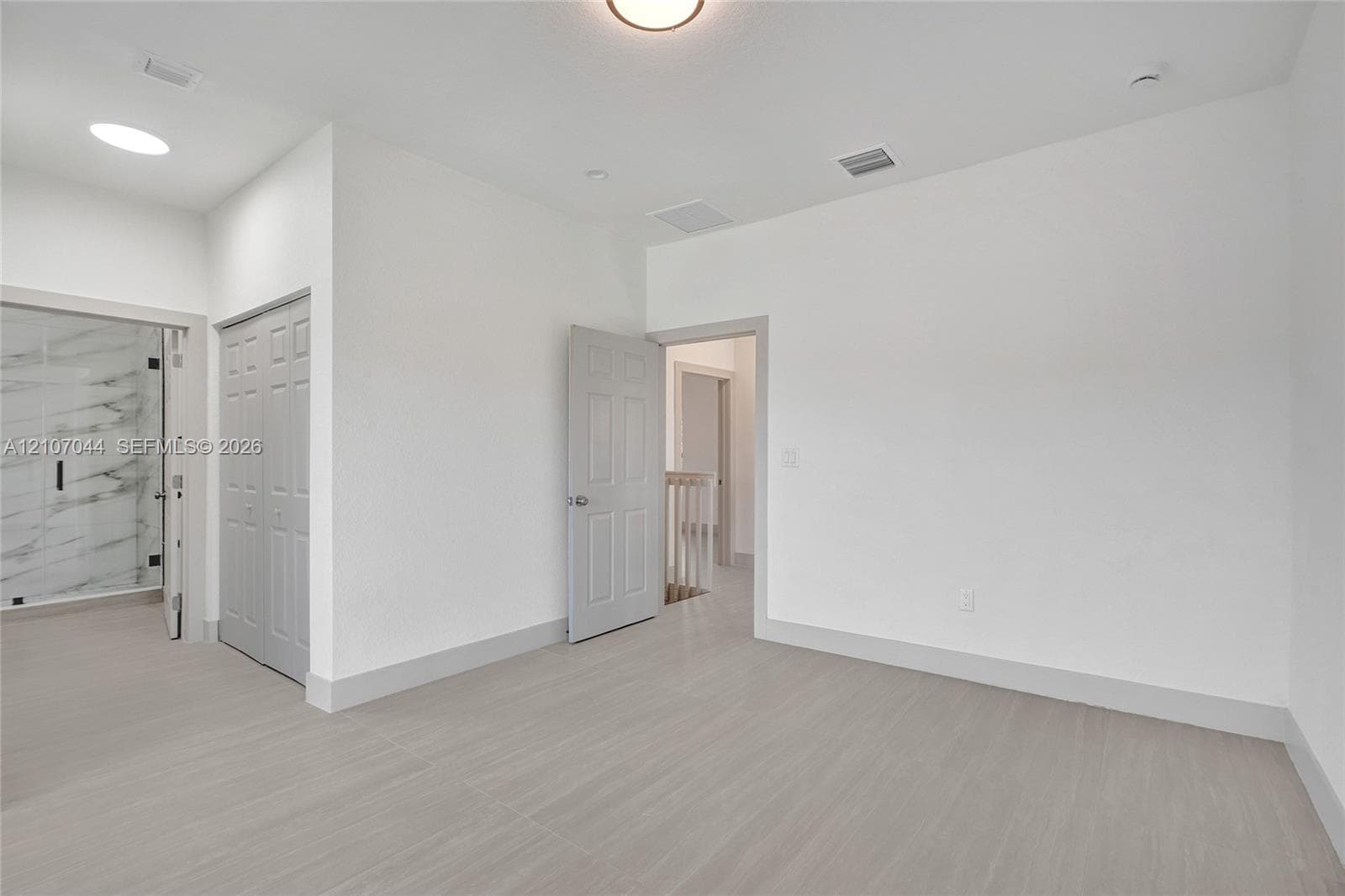 Neutral-toned wood-finish flooring, crisp white walls, recessed ceiling lighting, multi-panel doors, and a glass-enclosed shower with stone-patterned wall tile