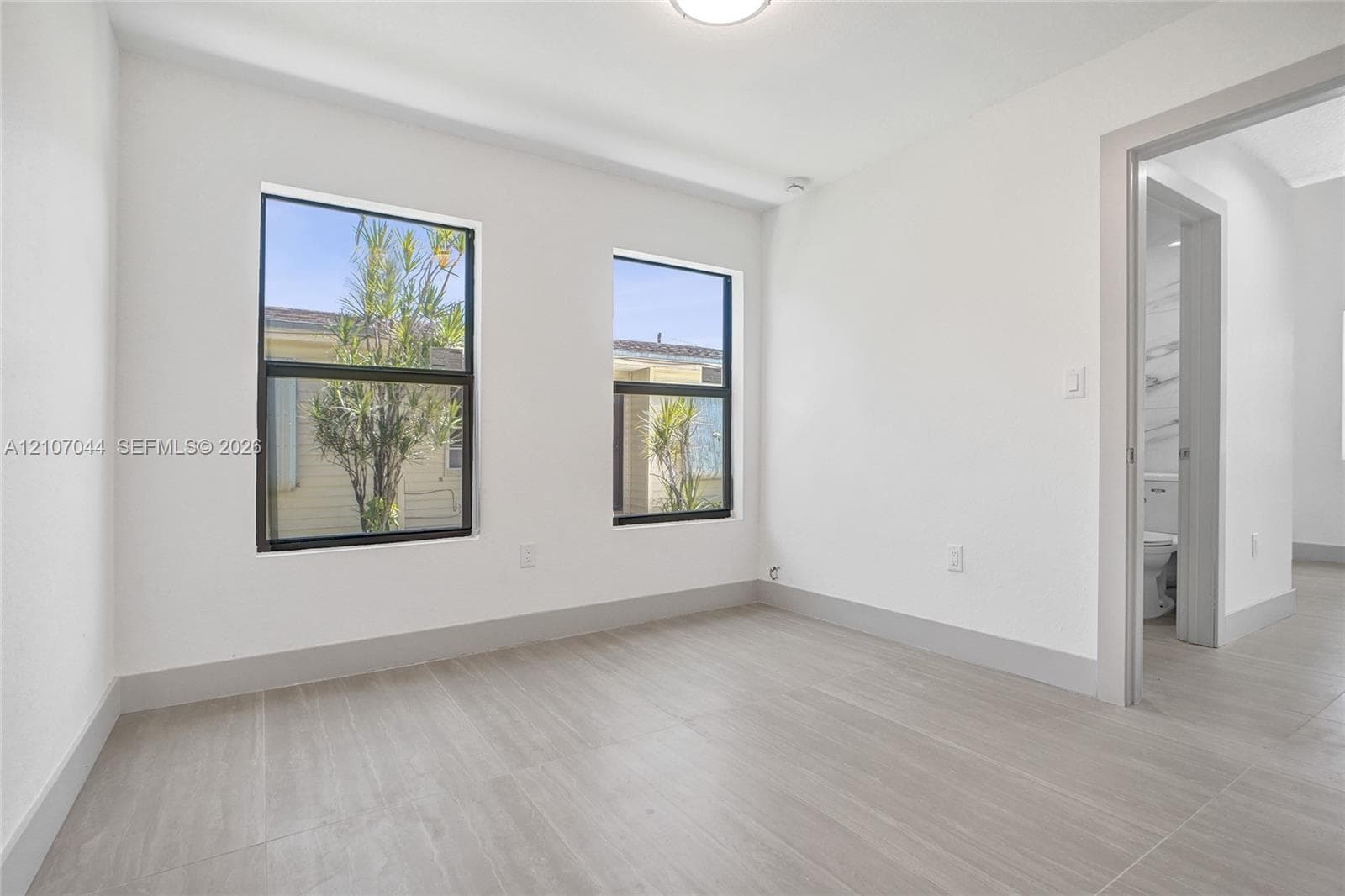 Neutral interior featuring wood-finish flooring, two dual-pane windows with dark frames, and white wall finishes