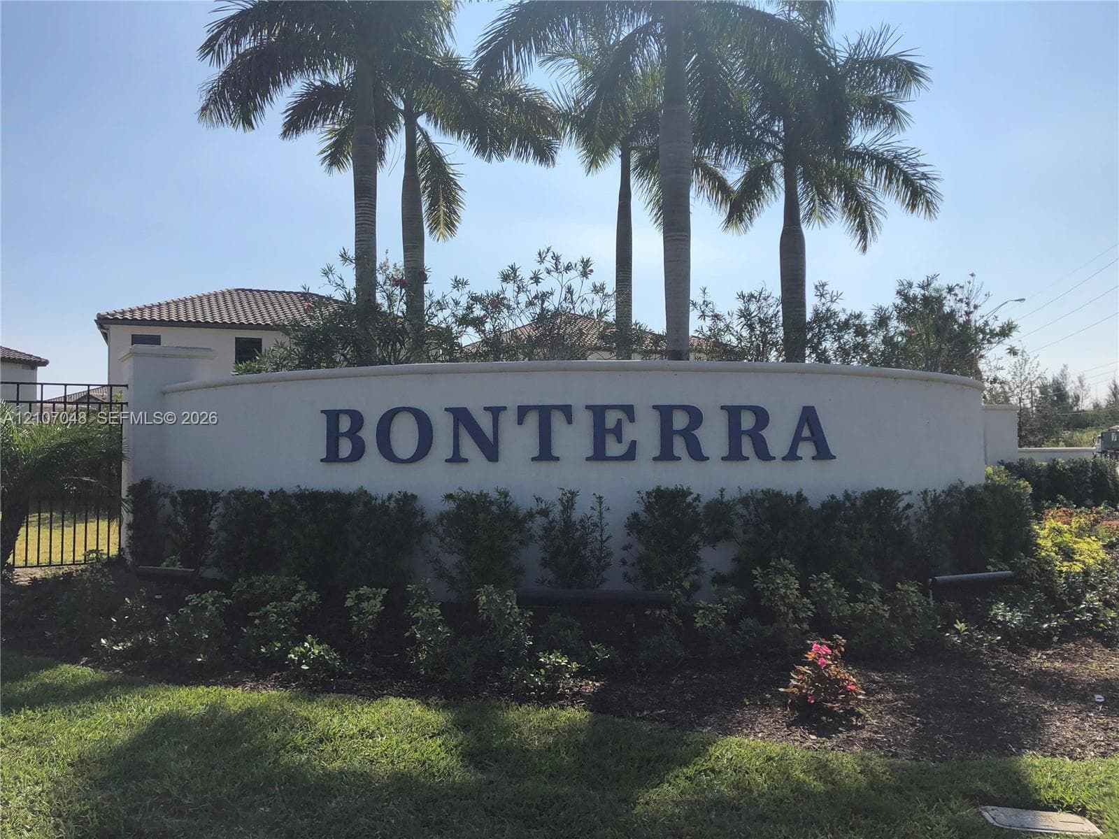 Curved monument signage featuring dimensional lettering, manicured hedges, and mature palm trees