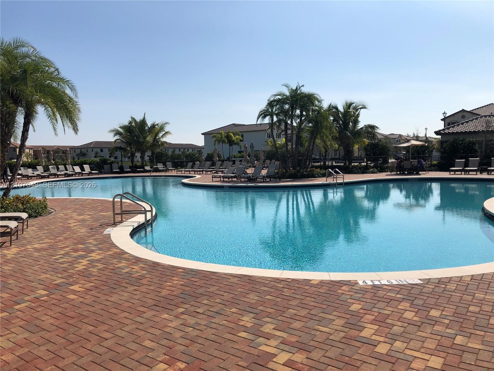 Resort-style swimming pool featuring brick paver decking, integrated metal handrails, and mature palm trees