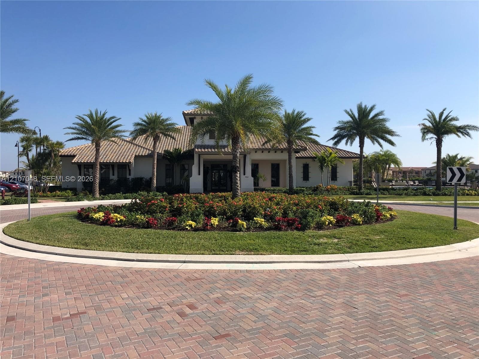 Stucco exterior featuring a multi-hipped tile roof, circular paver driveway, and mature palm tree landscaping