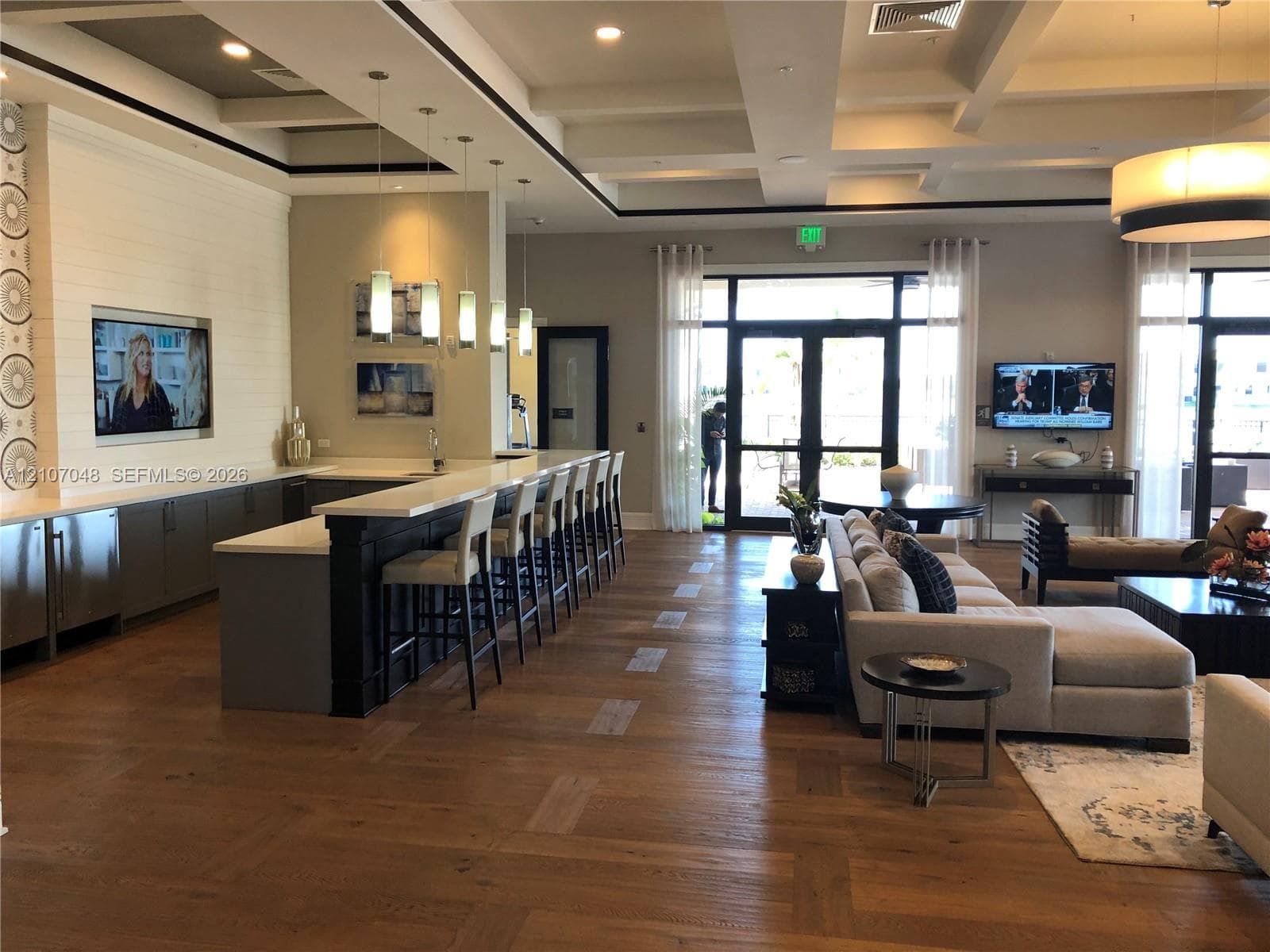 Spacious interior featuring a coffered ceiling, wood-finish flooring, built-in media cabinetry with wall paneling, and a kitchen island with stone countertops and pendant lighting