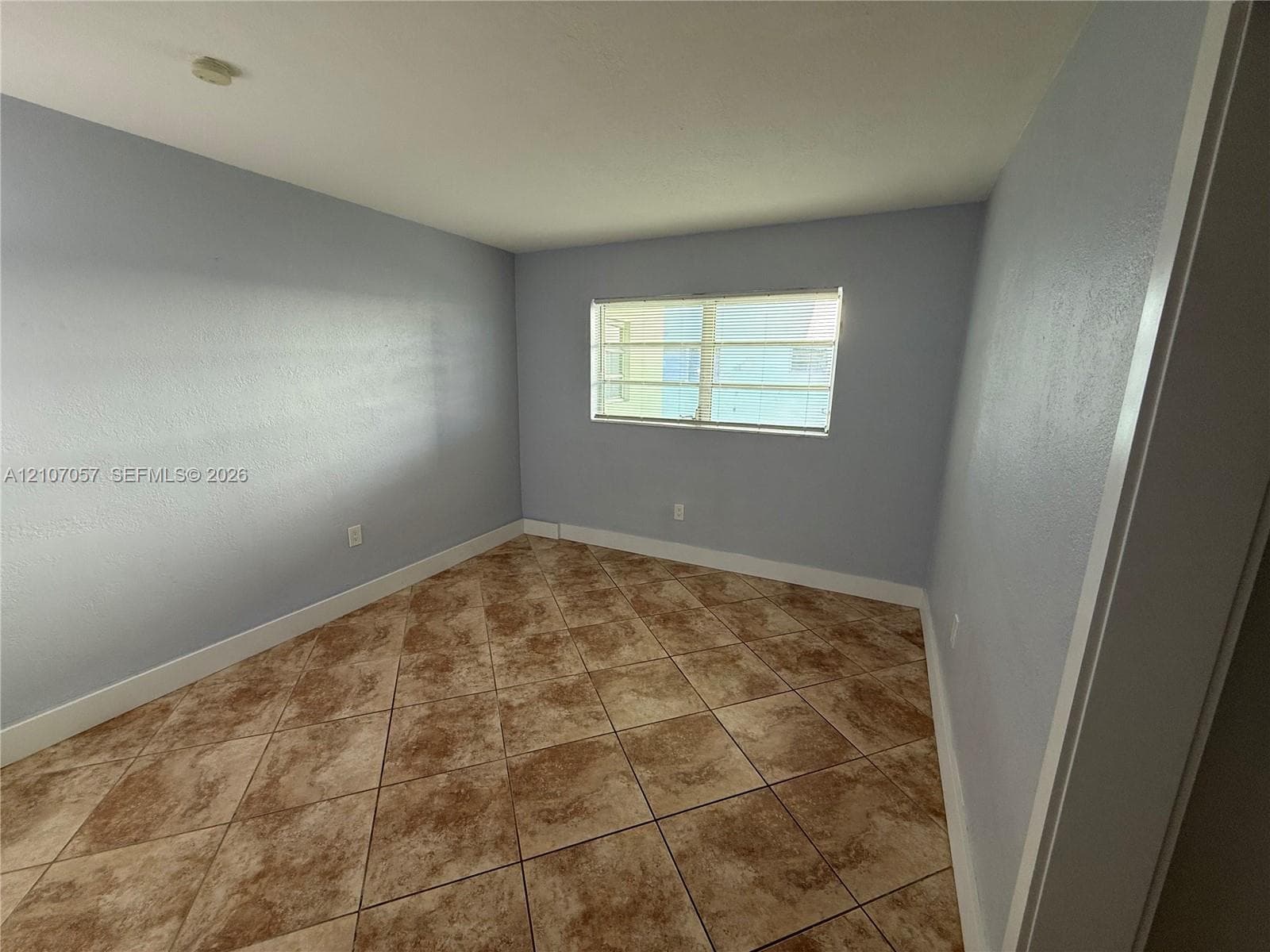 Interior room featuring neutral-toned wall paint, large-format diagonal tile flooring, and a single-pane window