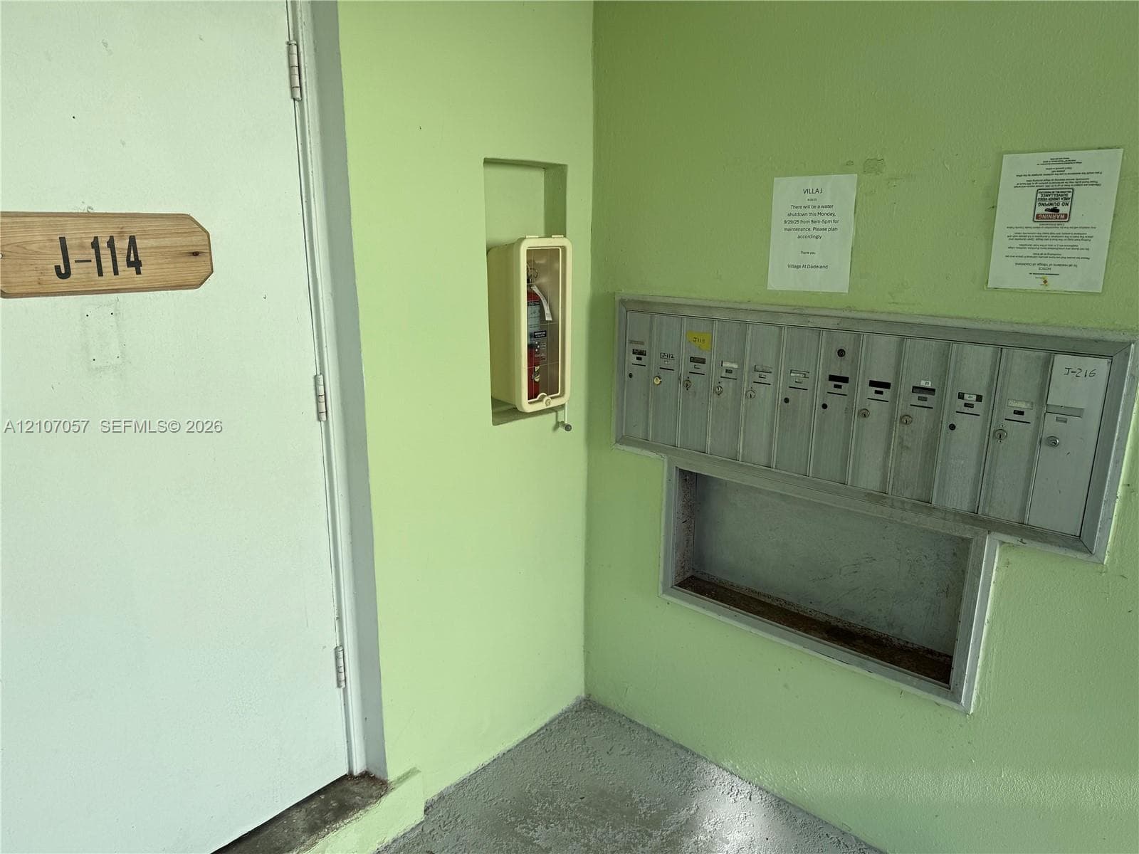 Wall-mounted metal mailbox bank, recessed fire extinguisher cabinet, and solid-core door with wooden unit number signage