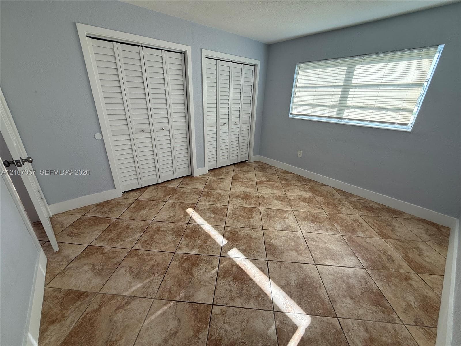 Tile flooring arranged in a diagonal pattern, two sets of white louvered-style closet doors, and a horizontal sliding window