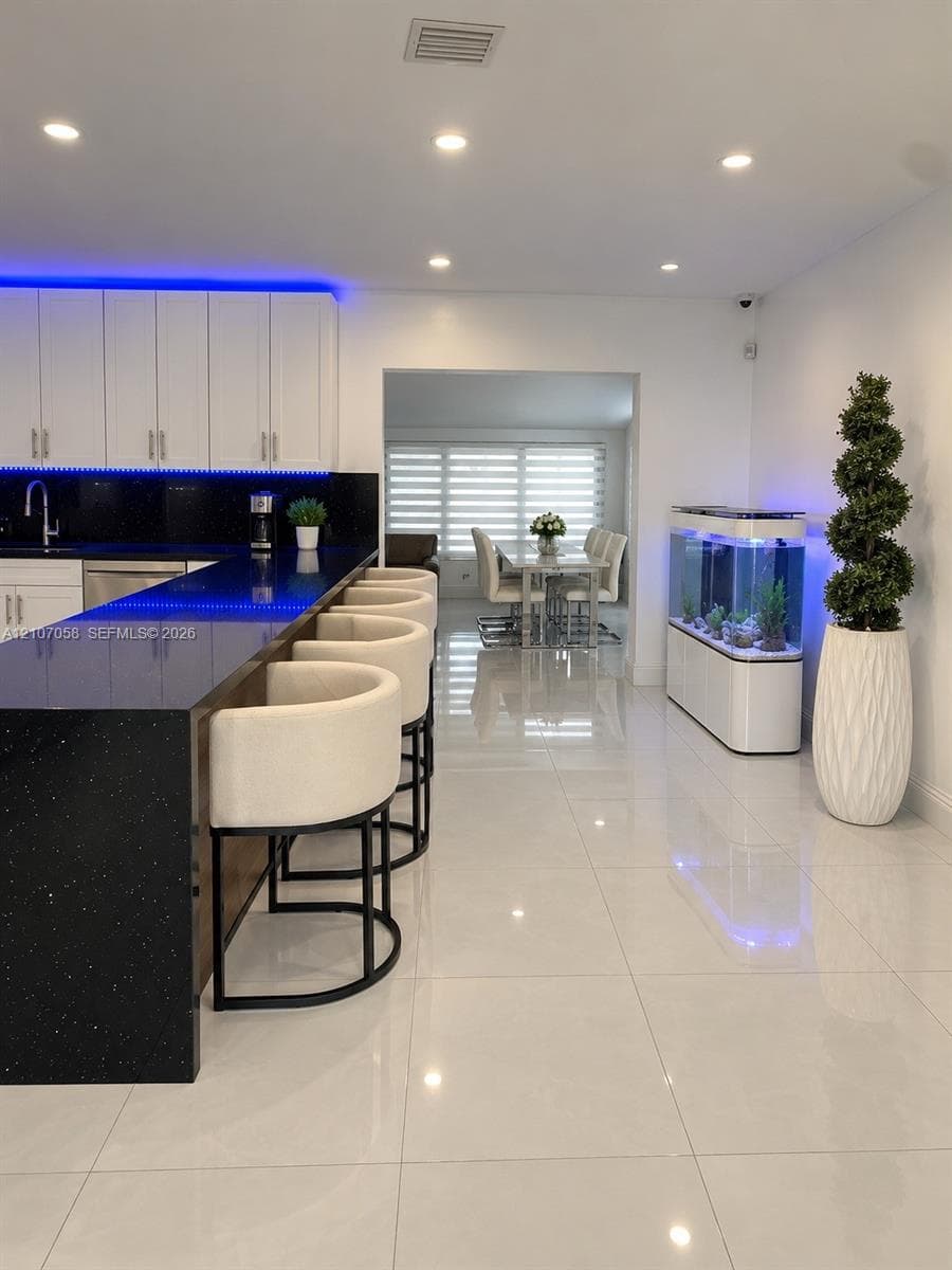 Modern kitchen featuring a breakfast bar with stone-finish countertops, white cabinetry, integrated under-cabinet lighting, and polished large-format tile flooring