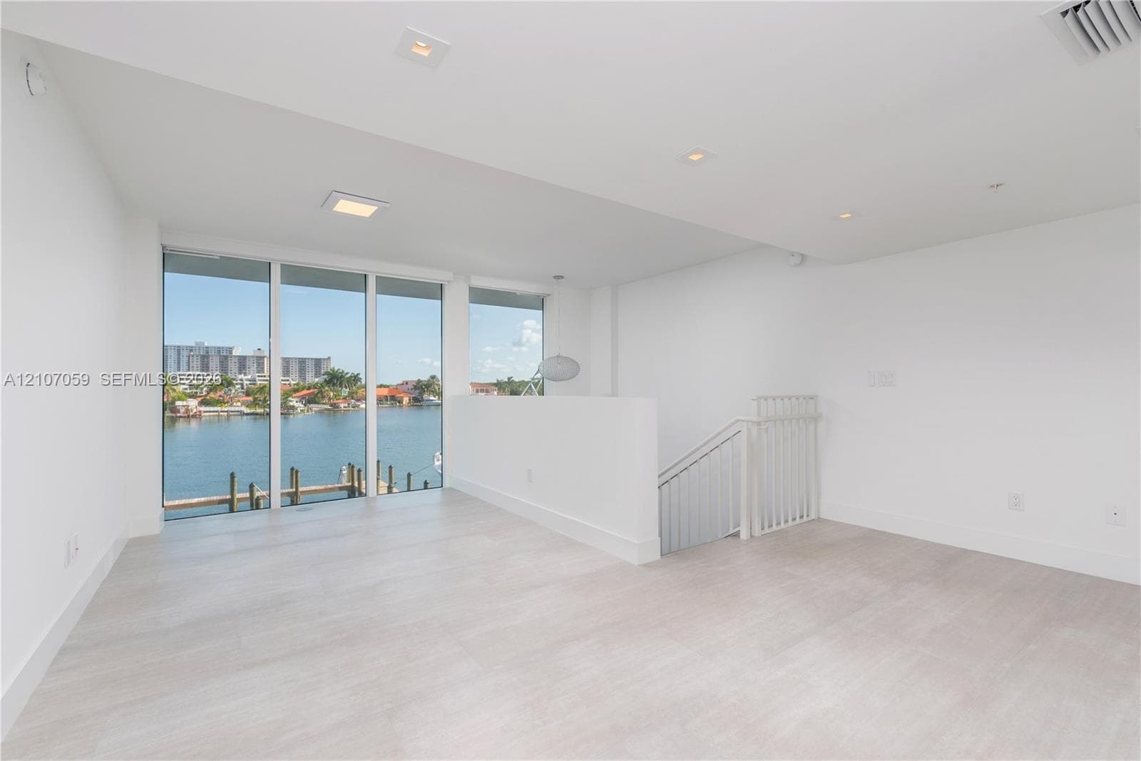 Open-concept interior featuring light wood-finish flooring, floor-to-ceiling windows, recessed lighting, and white railings