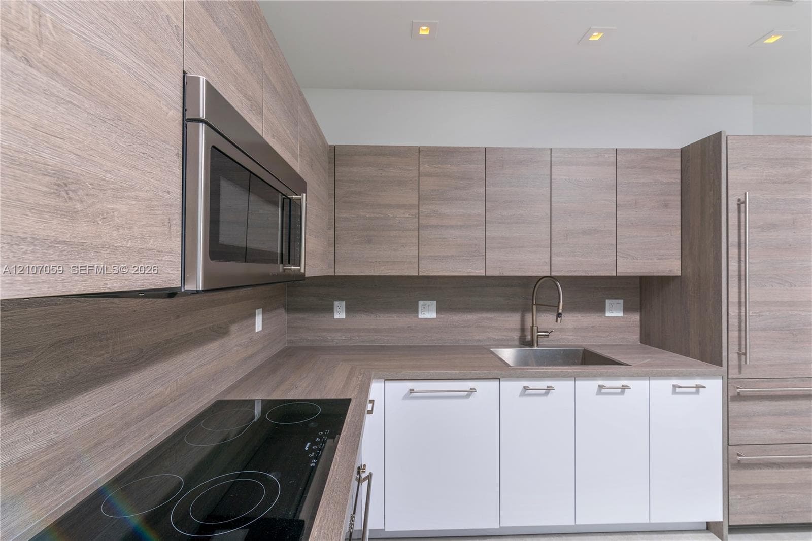 Kitchen featuring wood-finish cabinetry, integrated stainless steel appliances, a flush-mount electric cooktop, quartz-finish countertops, and a stainless steel under-mount sink with a gooseneck faucet