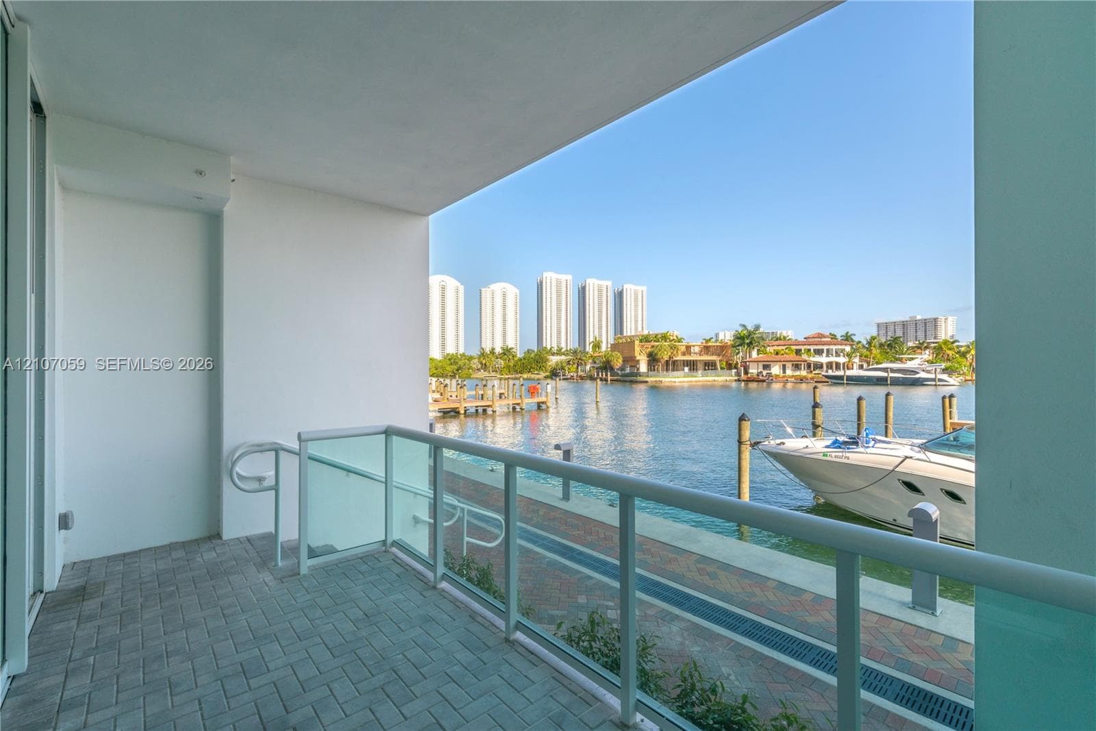 Covered balcony with brick paver flooring, glass railing system, and direct waterfront access