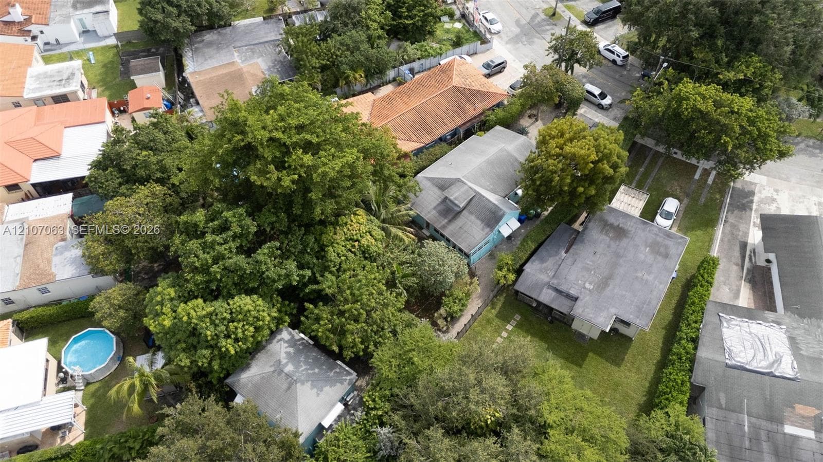 Aerial perspective of a residential lot featuring mature trees, landscaped grounds, concrete driveway, and shingle roofing