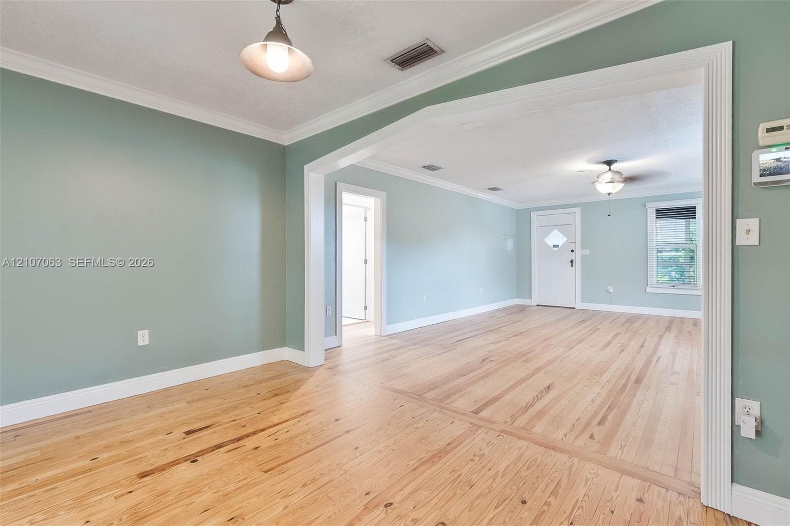 Interior space featuring wood-finish flooring, crown molding, a hanging pendant light, and a framed cased opening