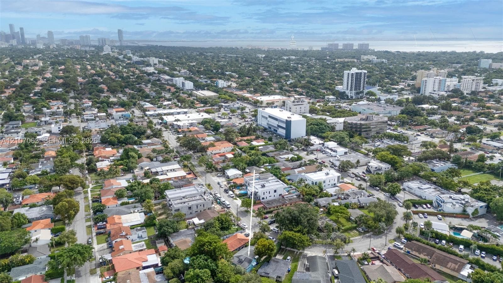 Aerial perspective featuring a residential lot situated within a grid of streets, mature canopy trees, and proximity to high-rise metropolitan infrastructure