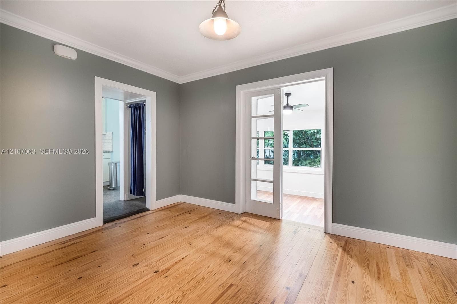 Room featuring wood-finish flooring, crown molding, a hanging pendant light, and a glass-paneled French door