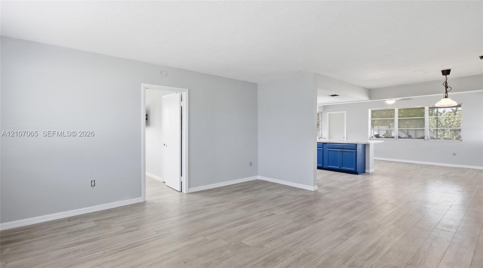 Open floor plan featuring wood-finish flooring, neutral wall paint, multi-pane windows, and a peninsula-style kitchen counter with blue cabinetry