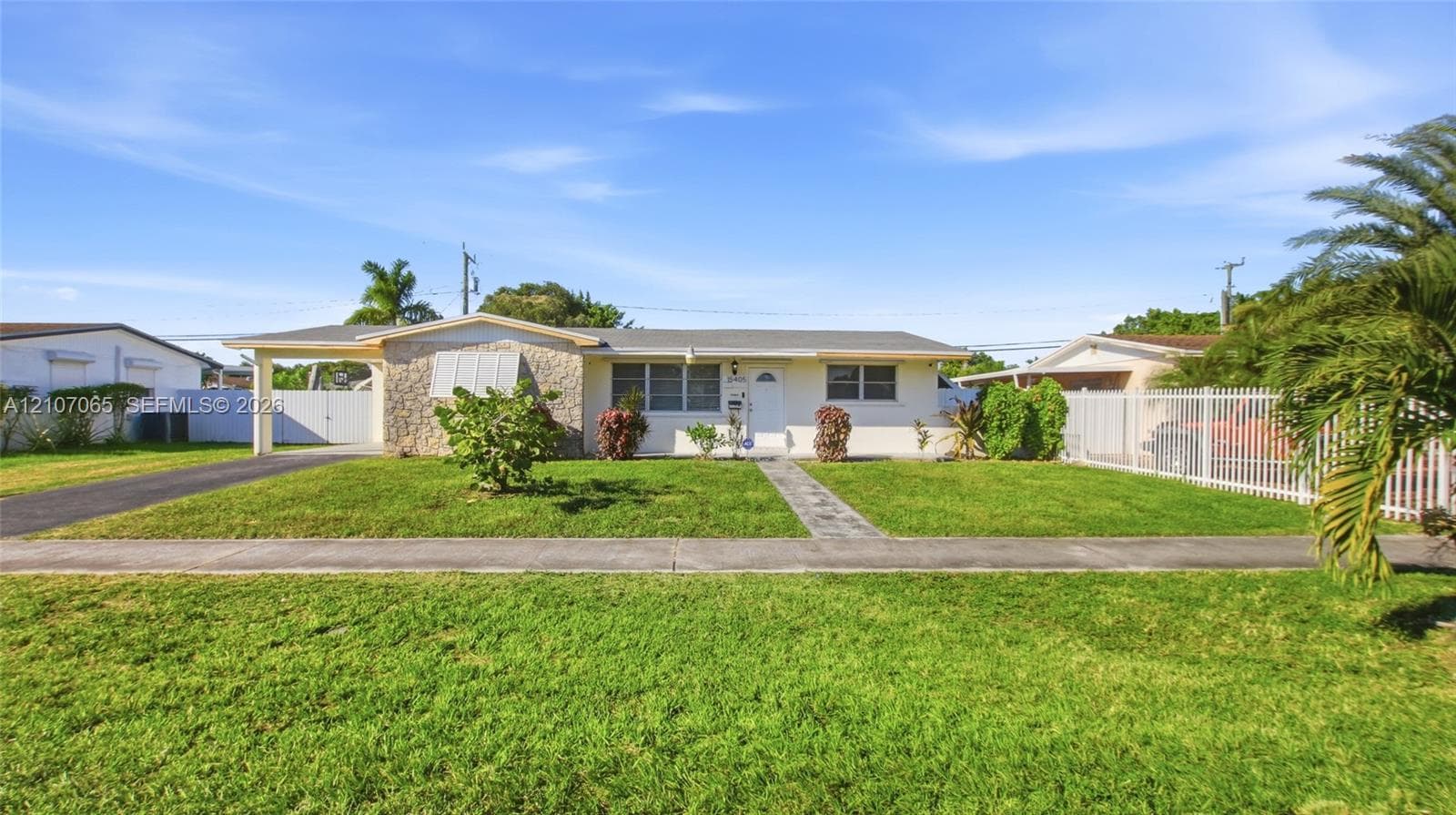 Single-story residence featuring a textured stone facade, attached covered carport, front lawn, and perimeter metal fencing