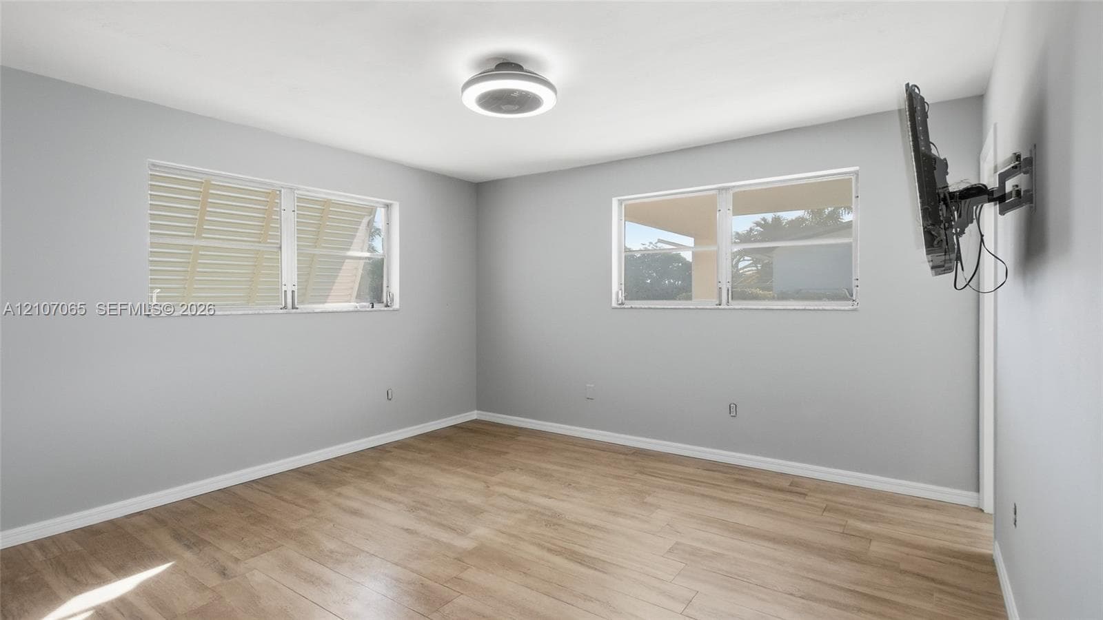 Neutral wall finishes, wood-finish flooring, two dual-pane windows, and a flush-mount circular LED light fixture