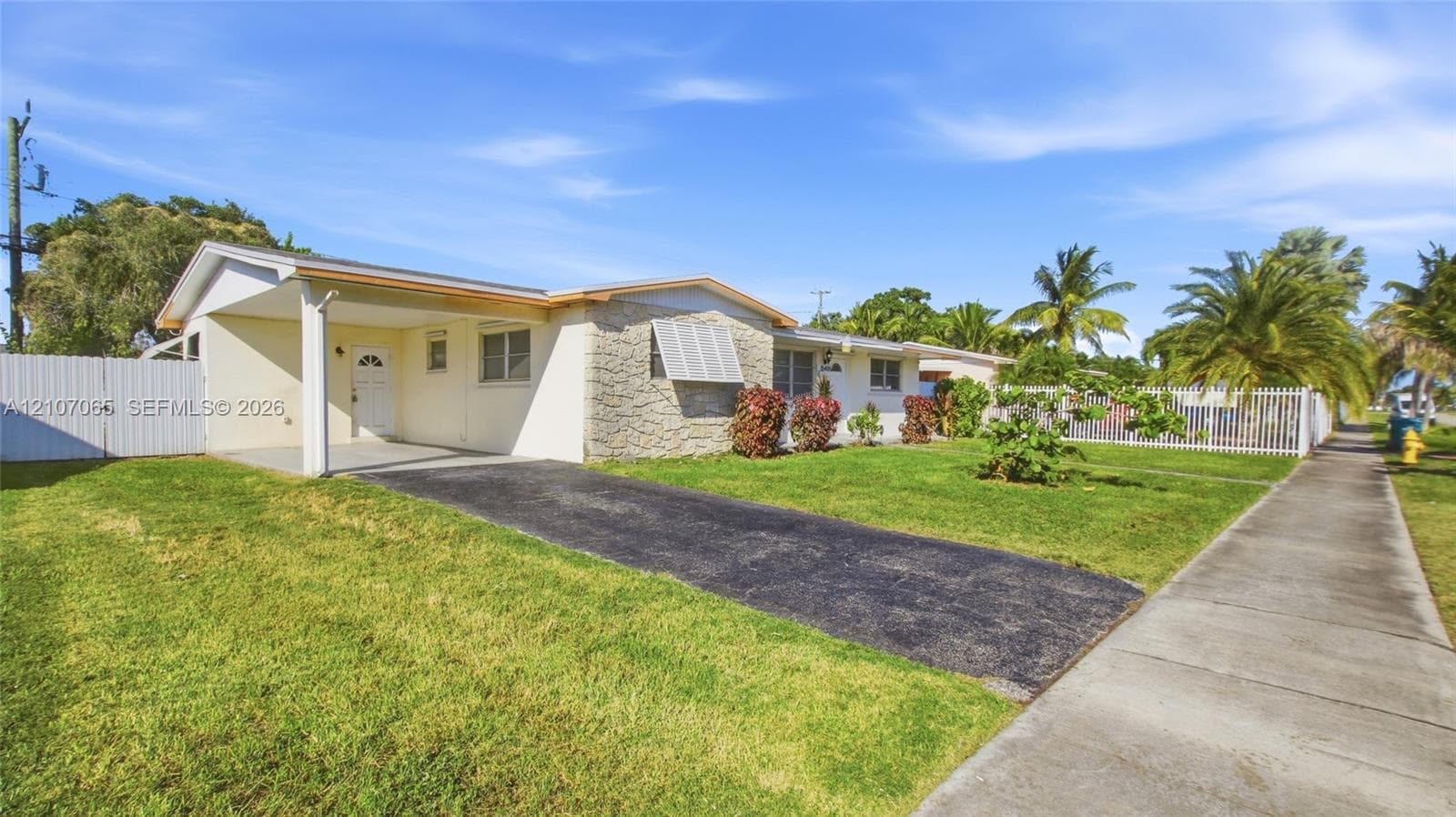 Single-story residence featuring a covered carport, stone facade detailing, and a white privacy fence encompassing the property grounds