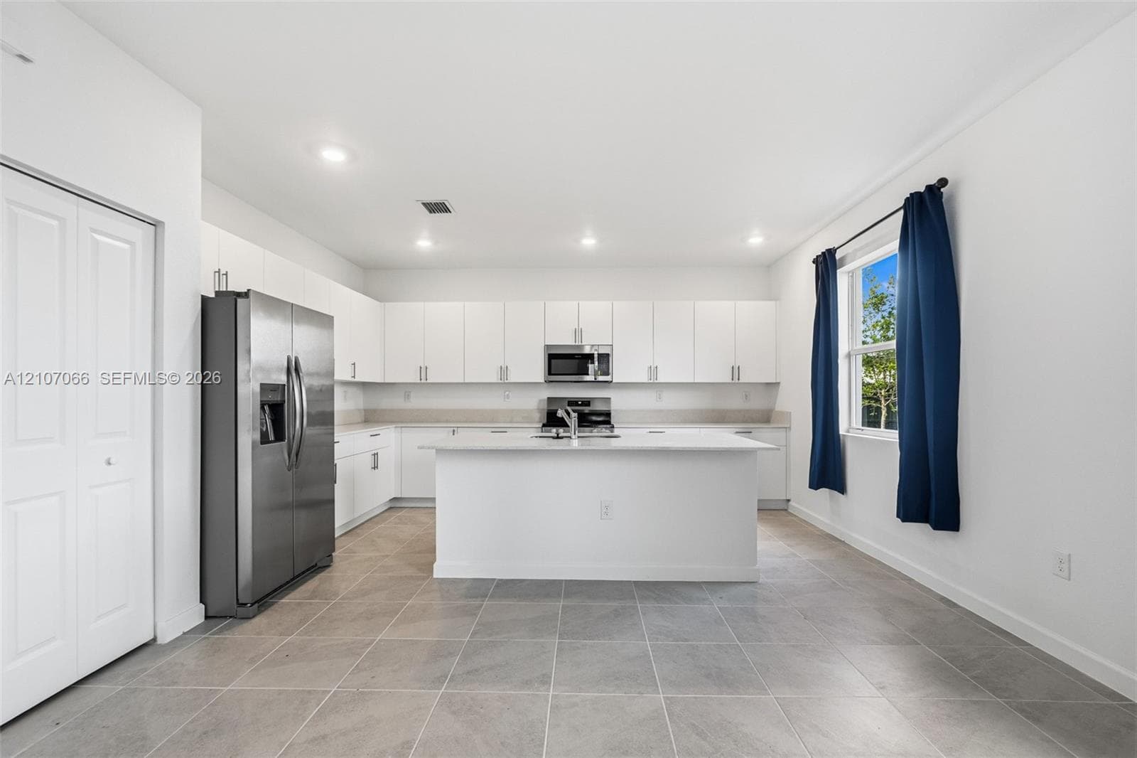 Kitchen featuring white flat-panel cabinetry, central island with stone-finish countertop, stainless steel appliances, and large-format tile flooring