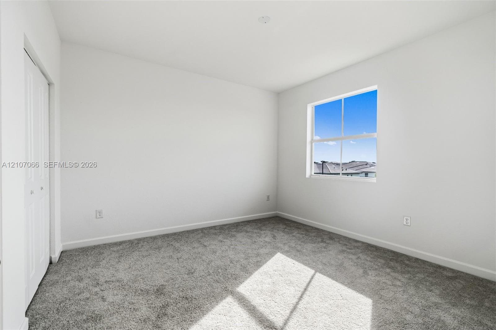 Neutral-toned wall-to-wall carpeting, single-pane window with white frame, and white bi-fold closet doors
