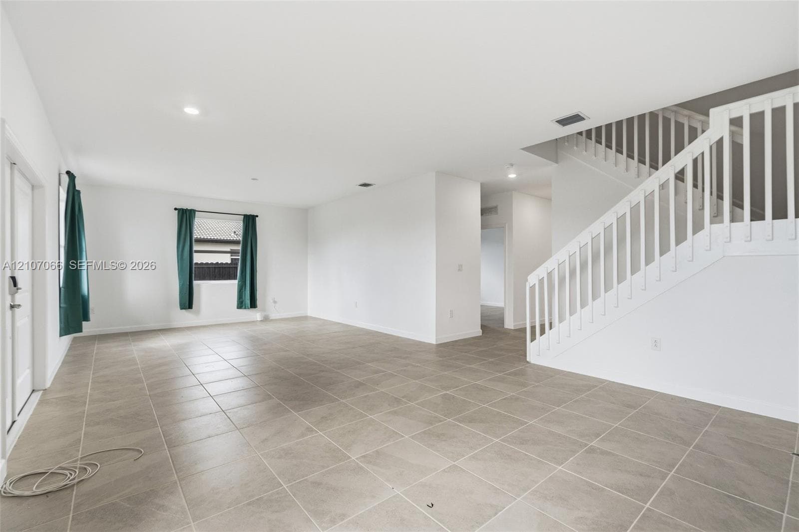 Open-concept interior featuring large-format ceramic tile flooring, recessed lighting, and a staircase with a white balustrade