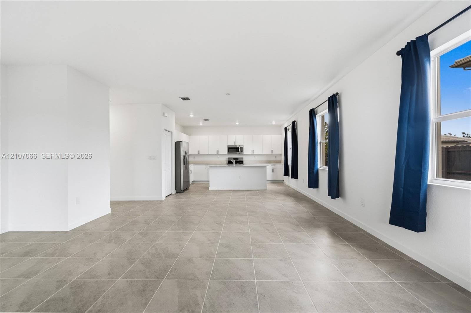 Open-concept area featuring oversized neutral tile flooring, white cabinetry, a center island, stainless steel appliances, and large windows