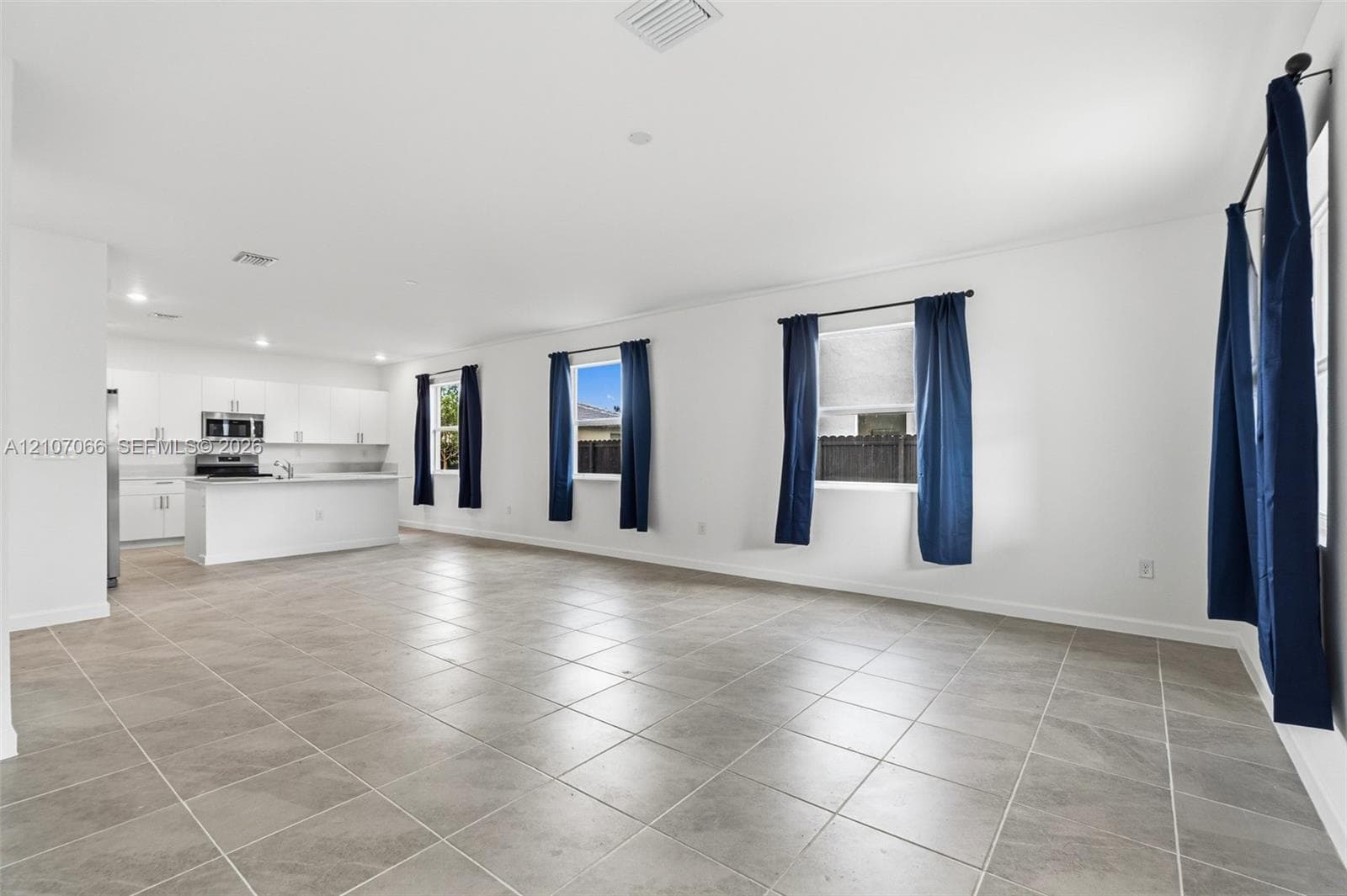 Open-concept area featuring large-format tile flooring, recessed ceiling lighting, and a kitchen equipped with white cabinetry, a central island, and a built-in microwave