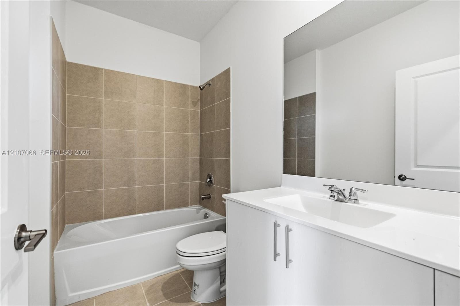 Bathroom featuring a white vanity with a composite countertop and integrated sink, a large wall-mounted mirror, and a tub-shower combination with full-height tile surround