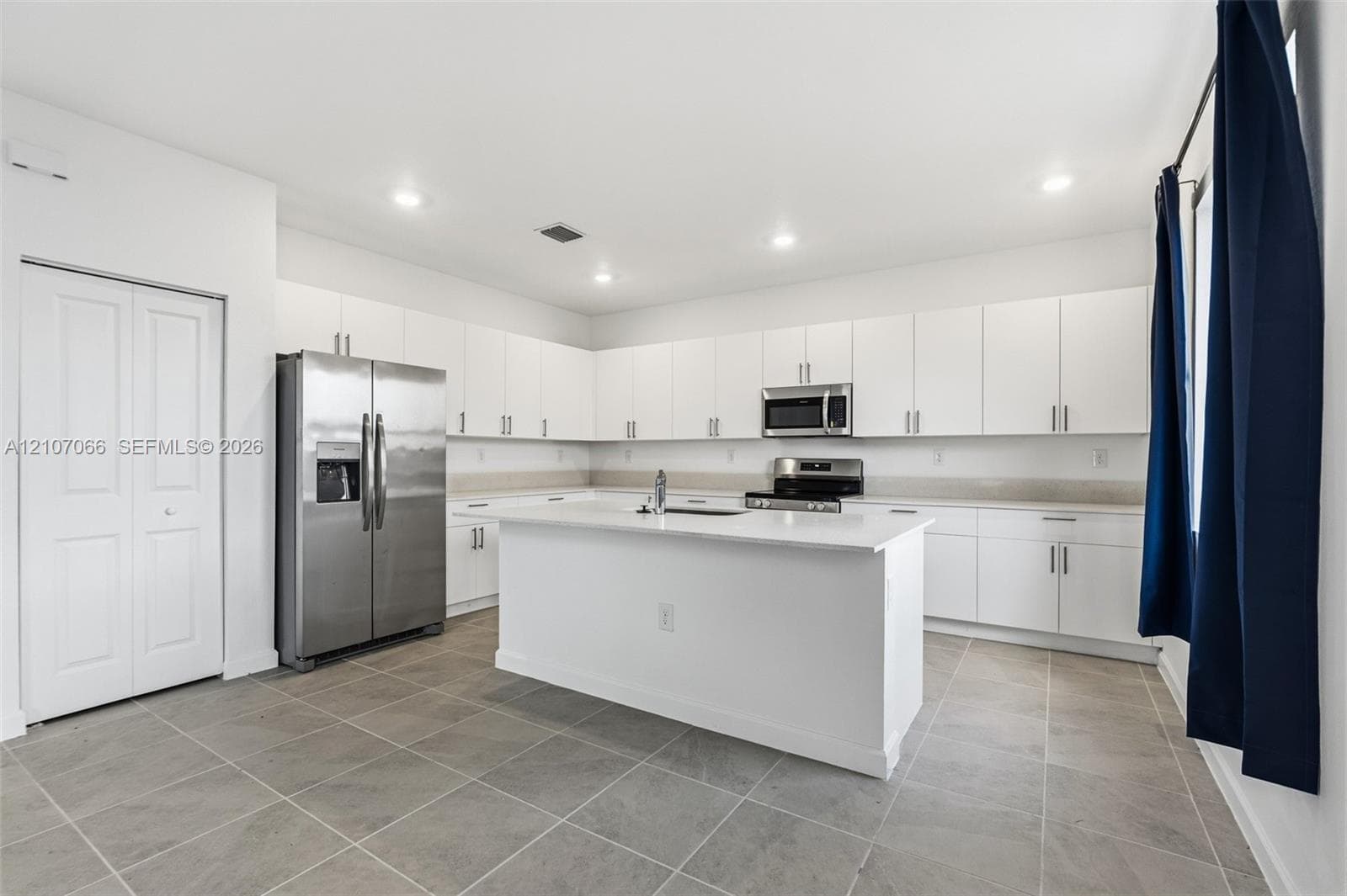 Kitchen featuring white cabinetry, center island with stone-finish countertop, stainless steel appliances, and tile flooring