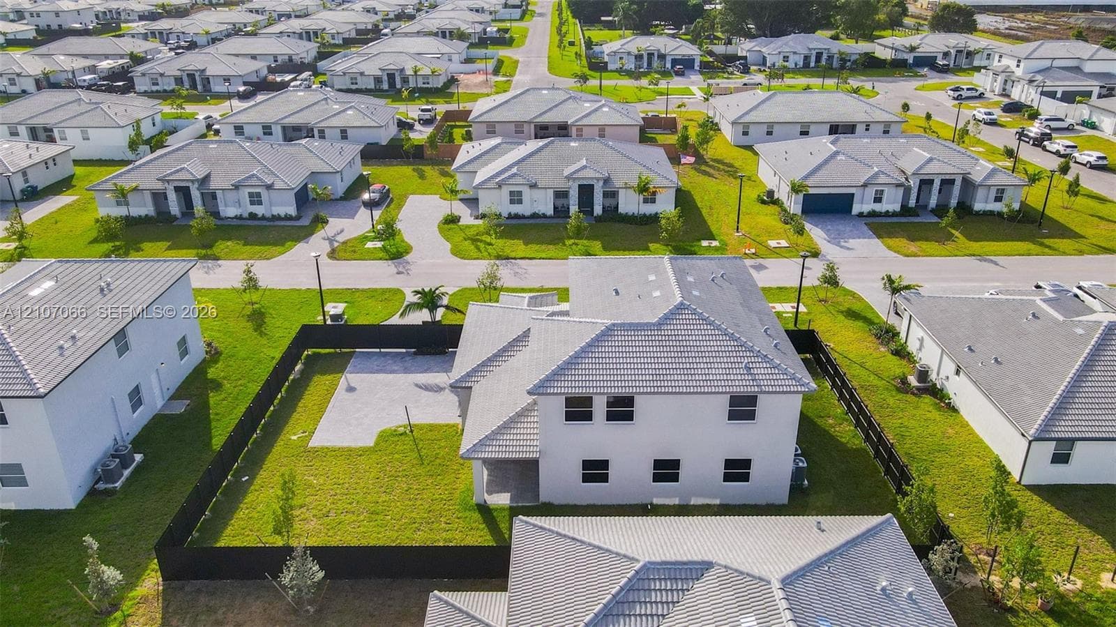 Two-story residence featuring a tile roof, paved rear patio, and a fully enclosed backyard with perimeter fencing