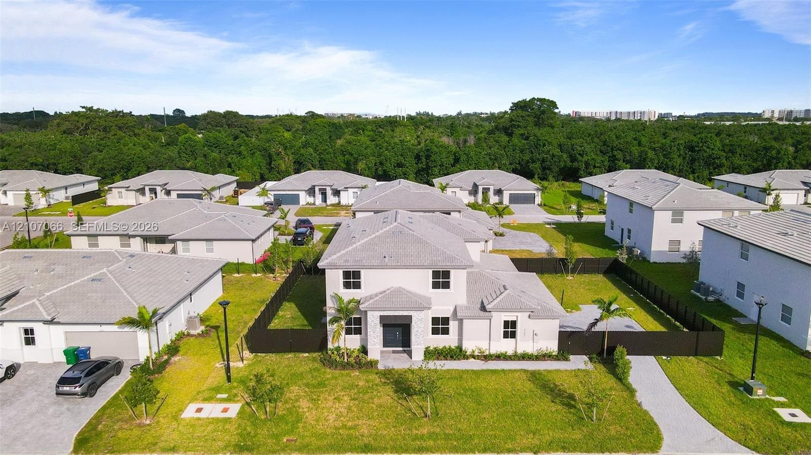 Two-story residence featuring a light-toned exterior, concrete tile roofing, dark-toned entry door, stone-accented facade, and a fenced backyard