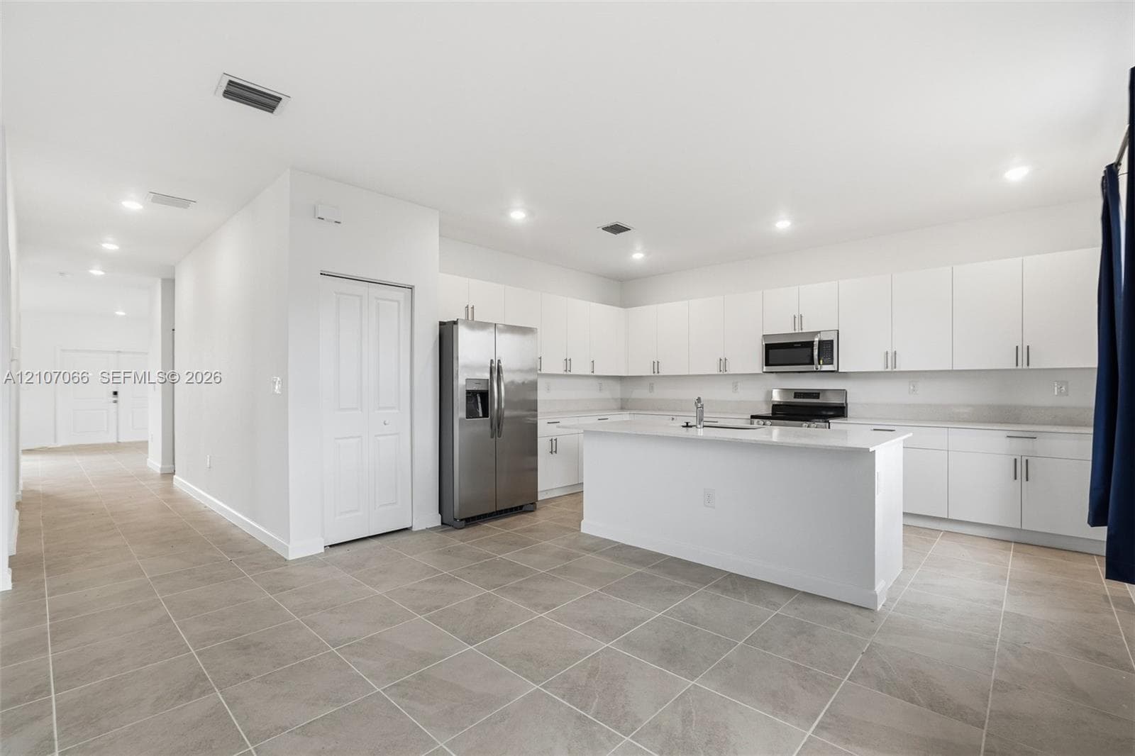 Kitchen featuring white shaker-style cabinetry, a central island with sink, stainless steel appliances, recessed lighting, and large-format tile flooring
