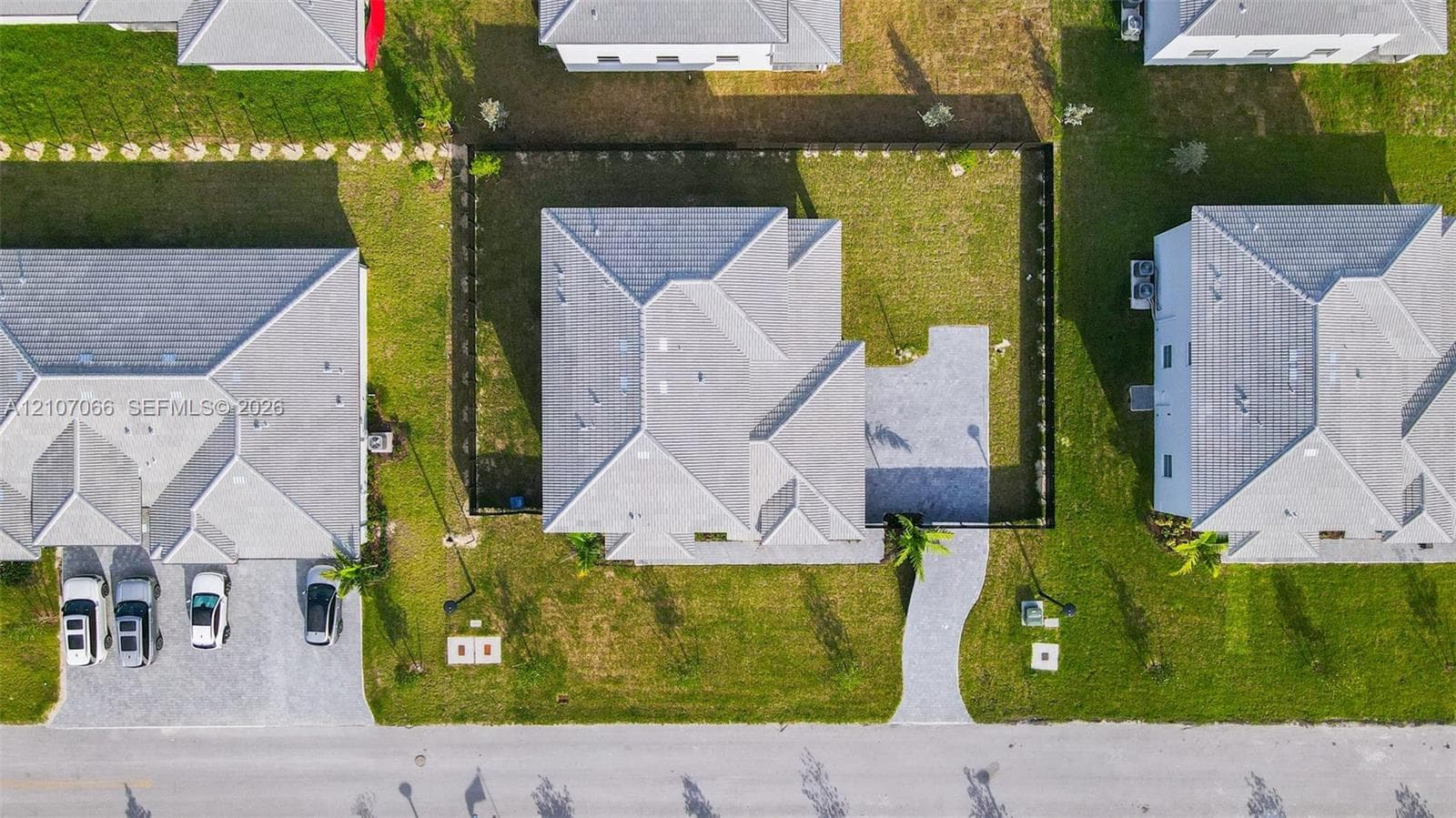 Aerial perspective featuring a hip-roof structure, paver walkway, fenced-in backyard, and expansive grass lot