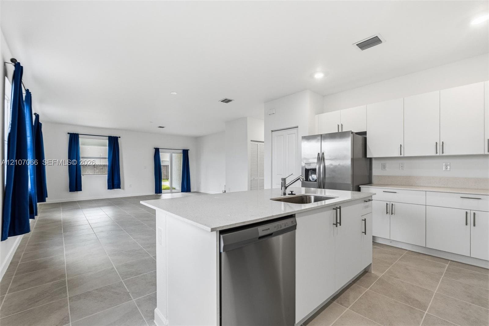 Kitchen featuring a central island with a stainless steel sink, flat-panel white cabinetry, stone-finish countertops, and stainless steel appliances, set against large-format tile flooring