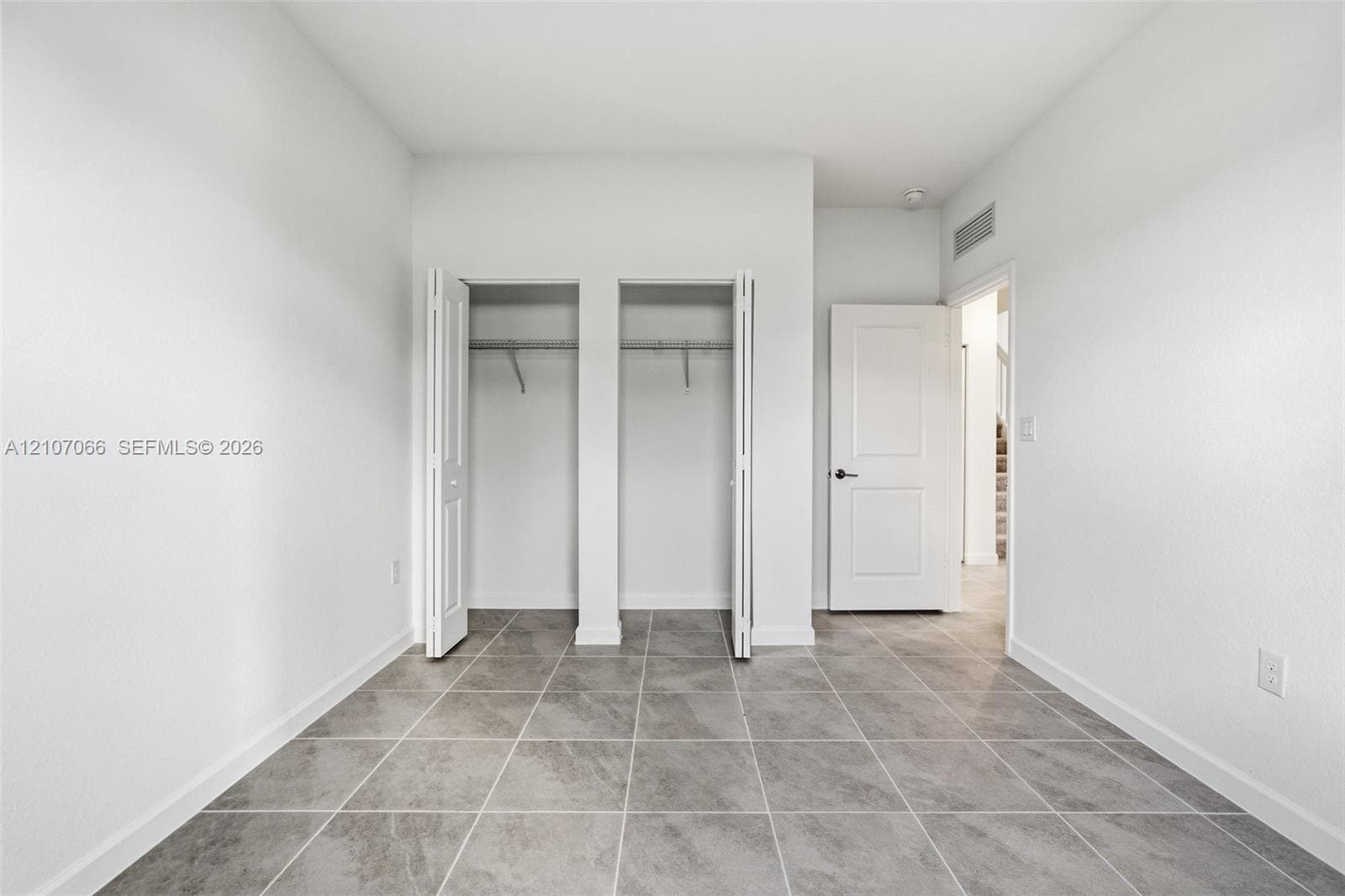 Room featuring large-format ceramic tile flooring, dual reach-in closets with bi-fold doors, and a solid-core interior door