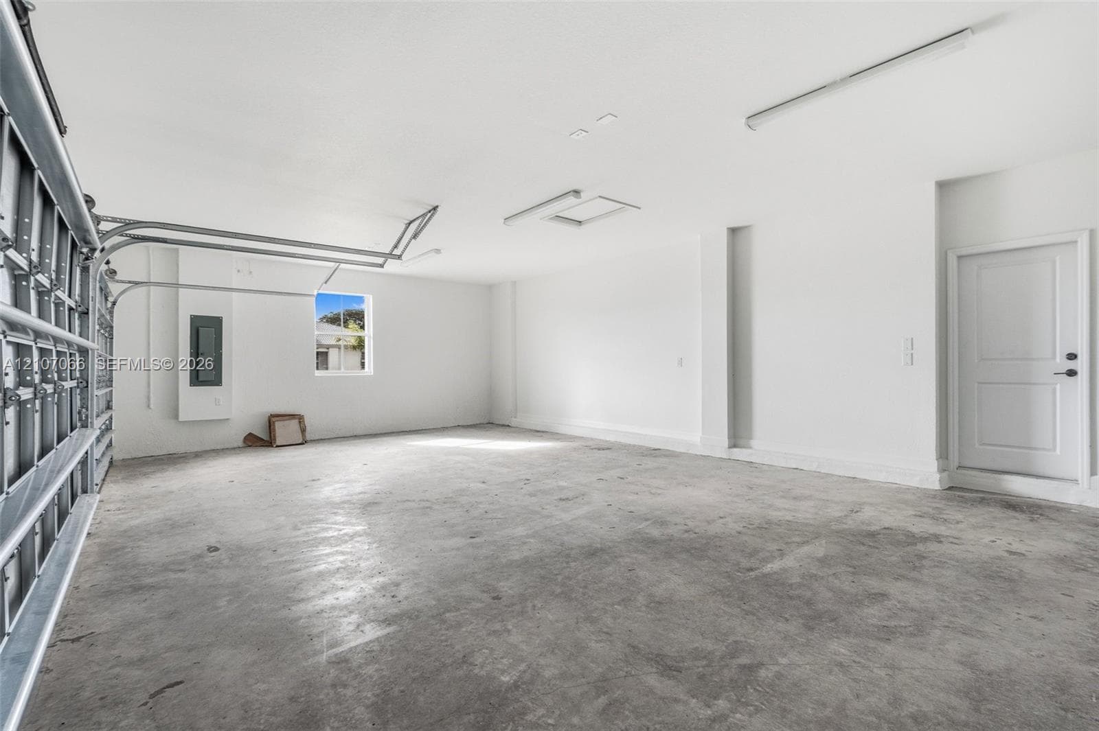 Spacious two-car garage featuring a concrete floor, high ceilings, linear overhead lighting, and an access door